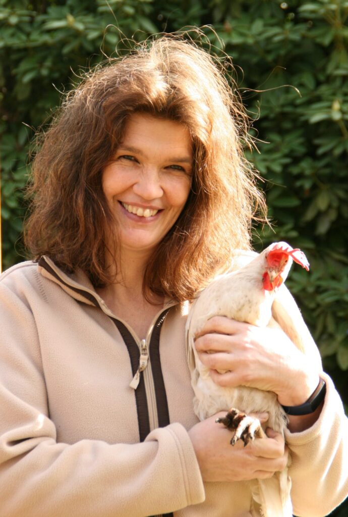 Porträt einer Tierheilpraktikerin mit einem Huhn im Arm als Symbol für achtsamen Umgang mit Tieren.